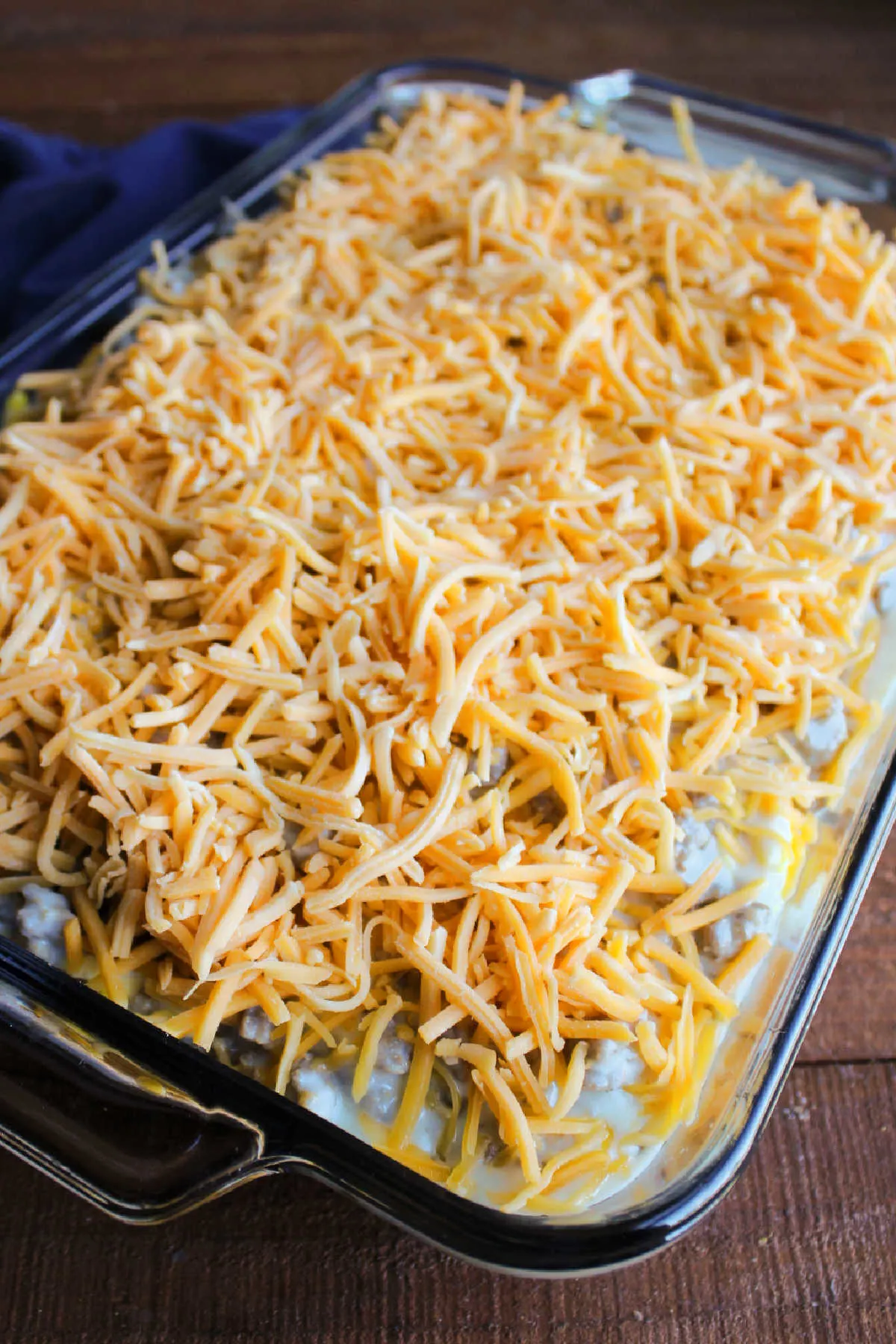 Shredded cheddar cheese layered over sausage gravy in casserole dish, ready to bake.