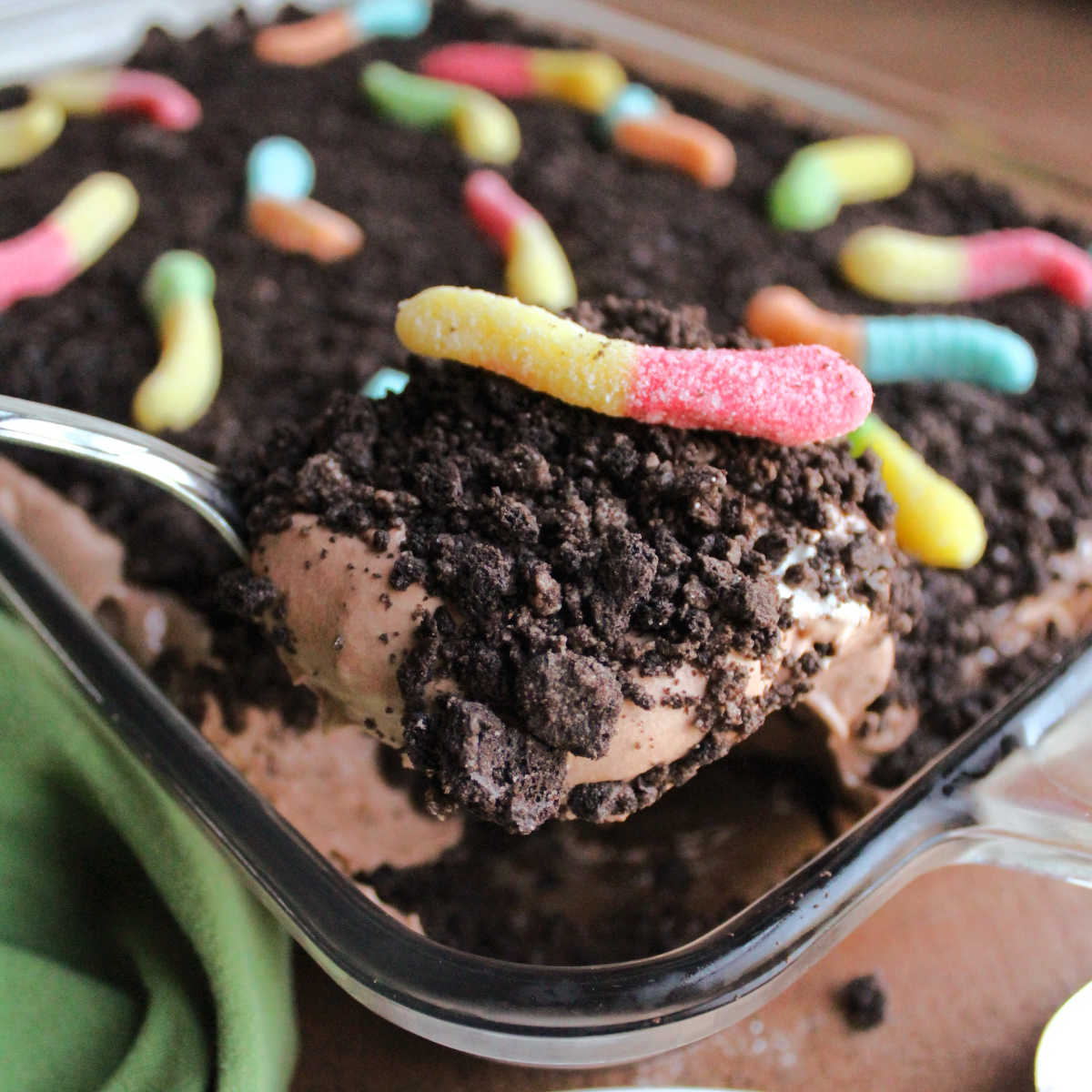 Serving spoon filled with dirt cake showing layers of Oreo crumbs, fluffy chocolate pudding mixture and sour gummy worms.