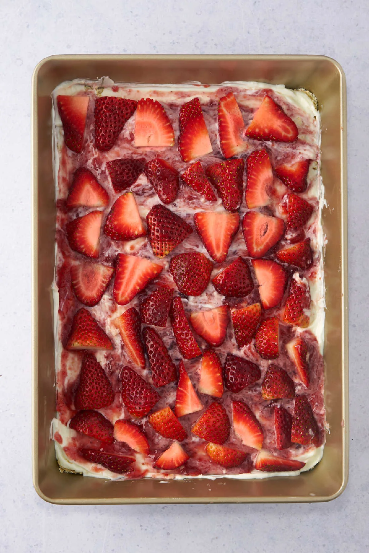 Fresh strawberry slices over yogurt and jam mixture in pan.