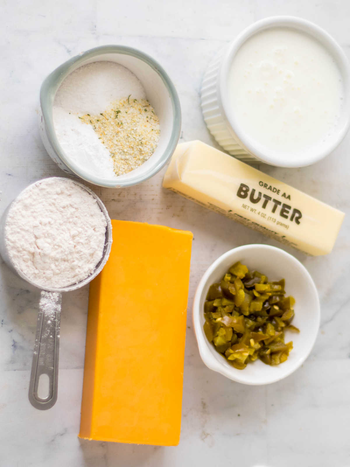 Ingredients including cheddar, jalapenos, butter, buttermilk, flour, baking powder, garlic salt and sugar ready to be made into butter swim biscuits.