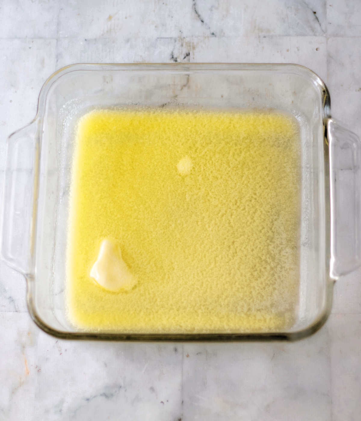 Square baking dish with melted butter inside.