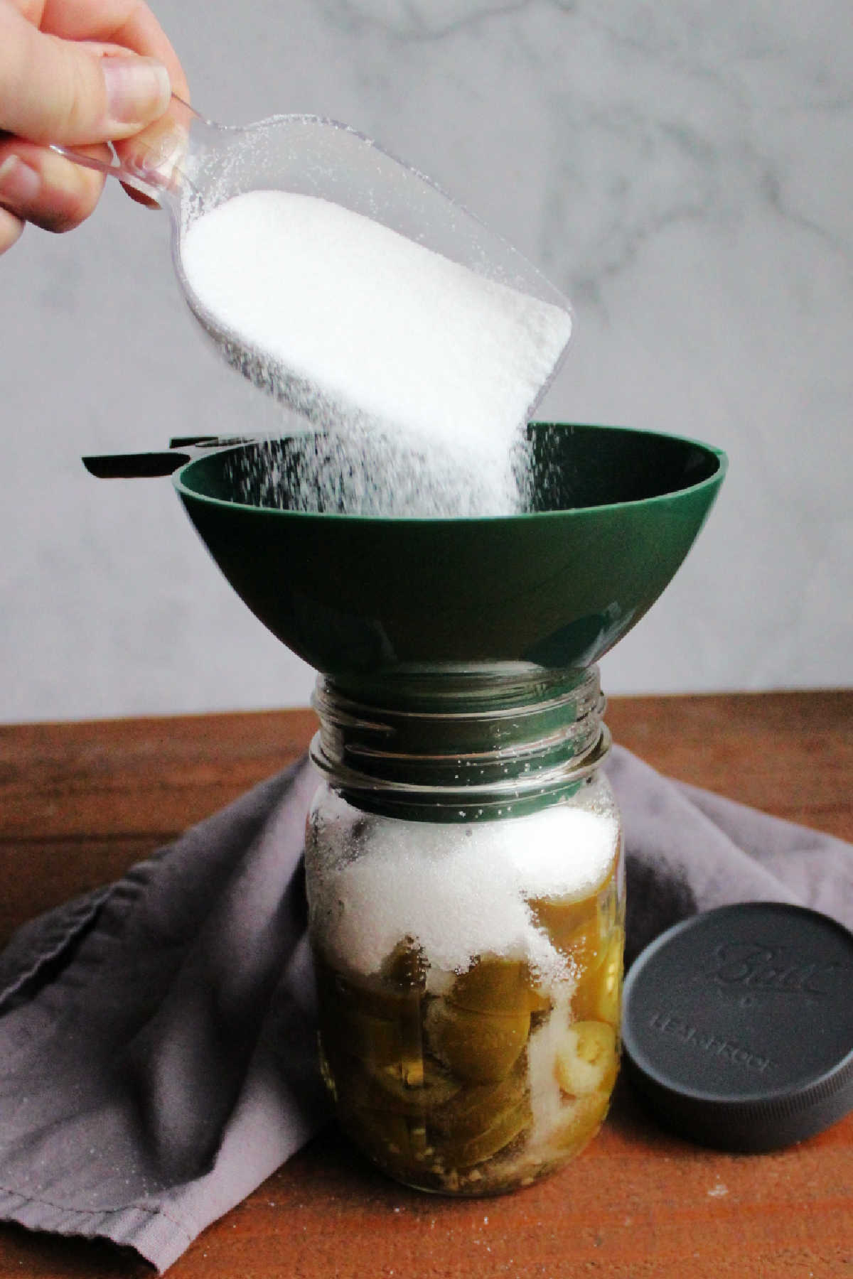 Pouring sugar into jar of pickled jalapenos.