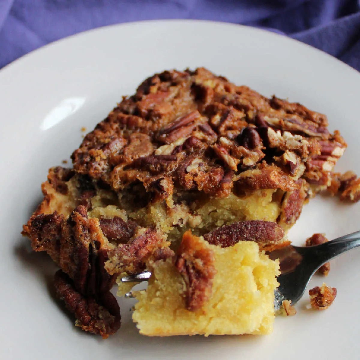 Bite of pecan pudding cake on fork showing dense texture of the cake layer topped with pecans and a crackly top.