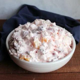 White serving bowl filled with fruit salad with fluffy pink dressing.