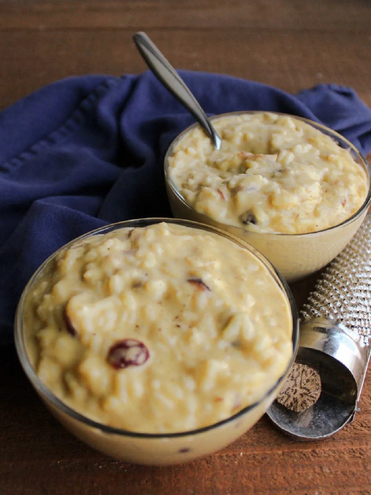 Close up of two small bowls of rice pudding showing creamy texture with rice and dried cranberries inside.