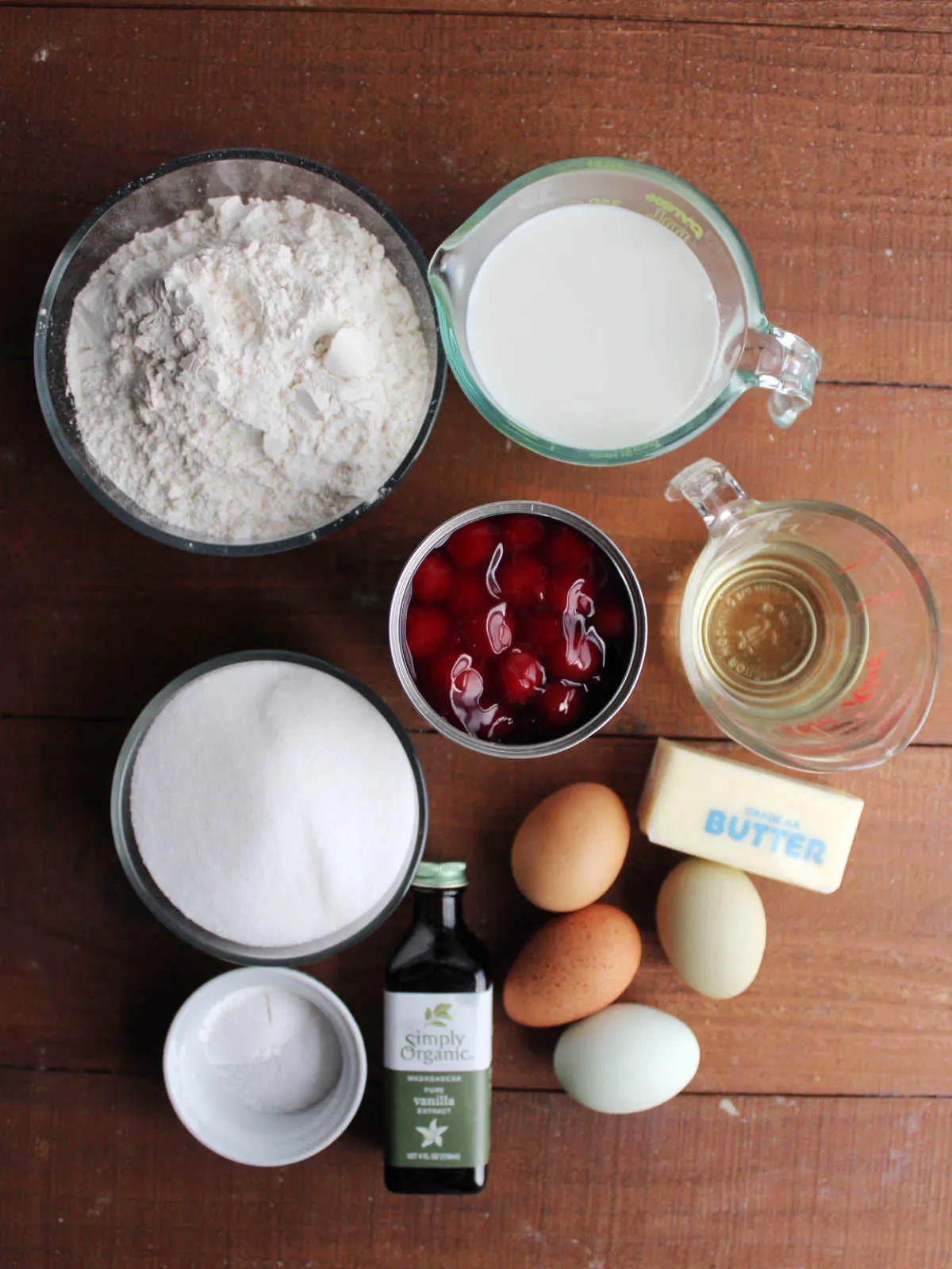 Ingredients including flour, sugar, milk, butter, eggs, oil, vanilla, baking powder, salt and cherry pie filling ready to made into cupcakes.