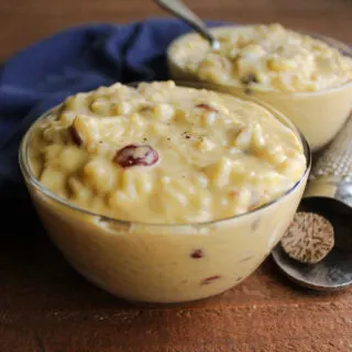 Close up of small glass bowls filled with creamy rice pudding with cinnamon, nutmeg and dried cranberries inside.