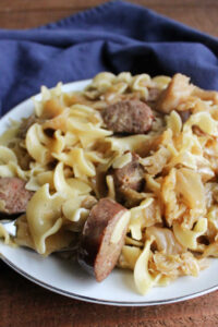 Plate of egg noodles, cabbage and sausage, ready to eat.