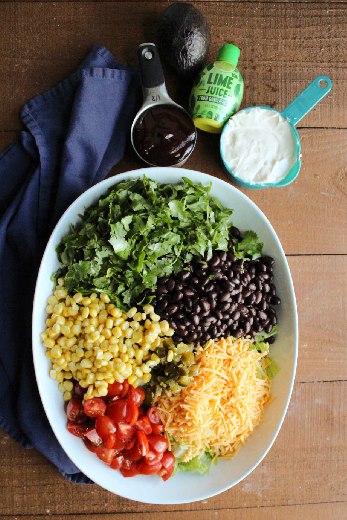 Large bowl of lettuce topped with various toppings including corn, beans, cheese, and tomatoes with the dressing ingredients in the background.