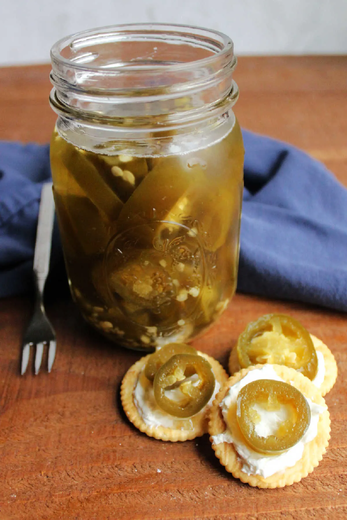 Crackers topped with cream cheese and candied jalapeno rings next to jar of cowboy candy.