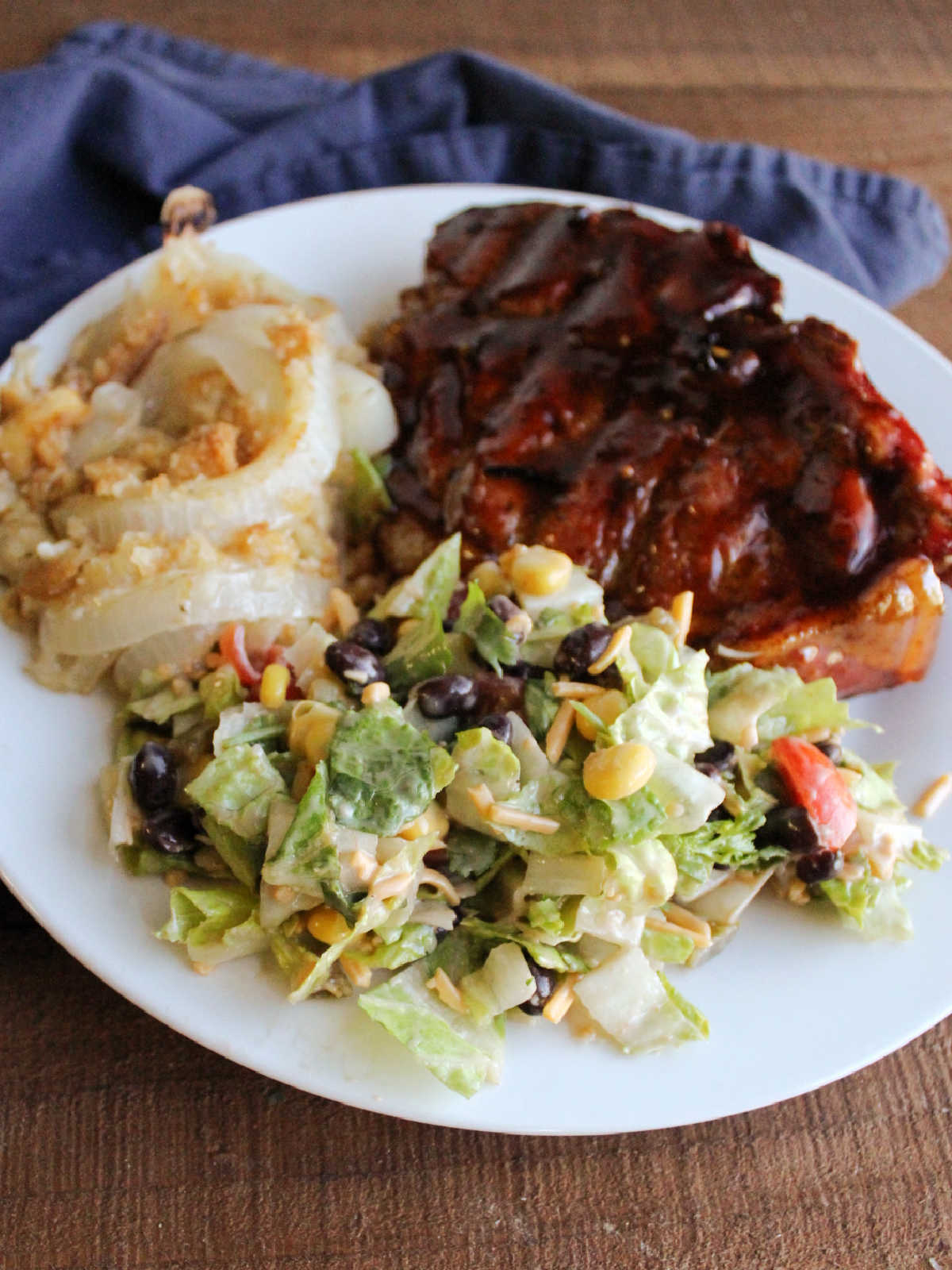Cowboy salad on dinner plate served with a bbq pork chop and cheesy onion casserole.