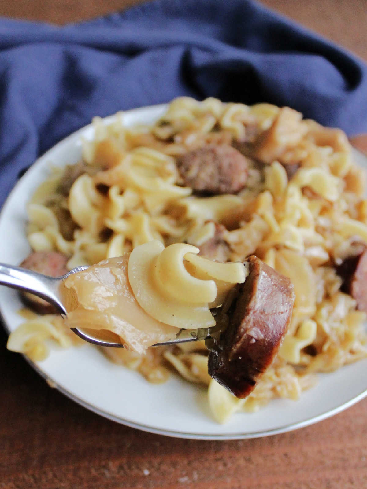Fork with egg noodles, cabbage and kielbasa on it, ready to eat. 