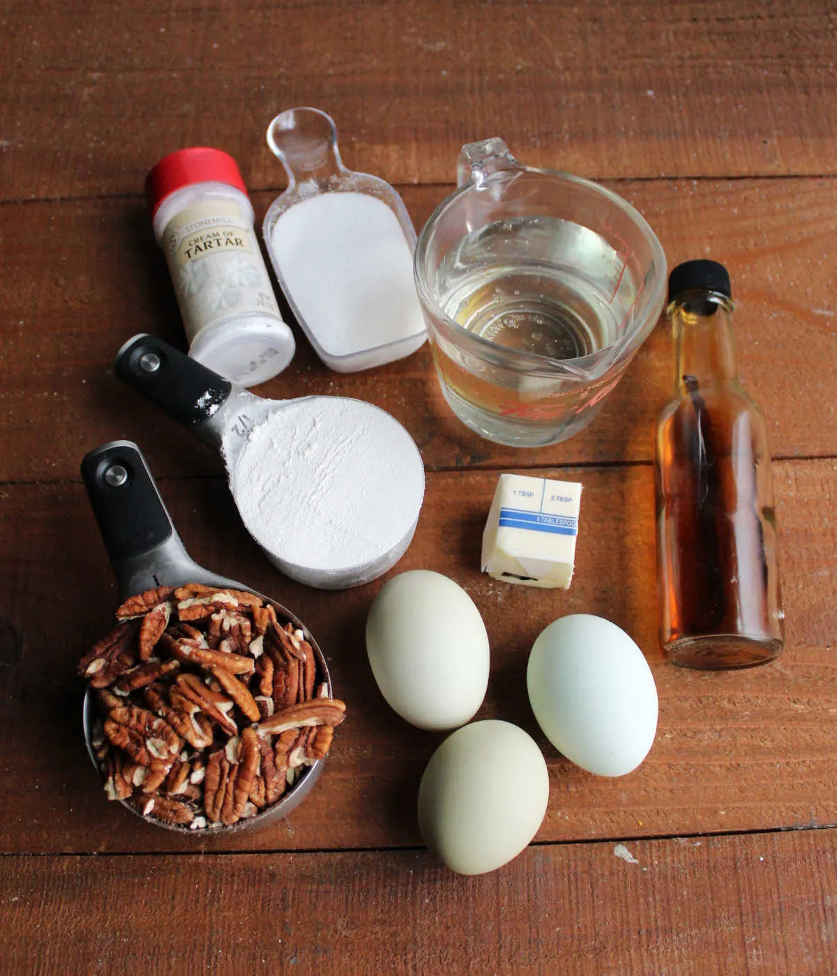 Ingredients including pecan, flour, eggs, sugar, corn syrup, butter, cream of tartar, and vanilla ready to be made into pecan pudding cake.