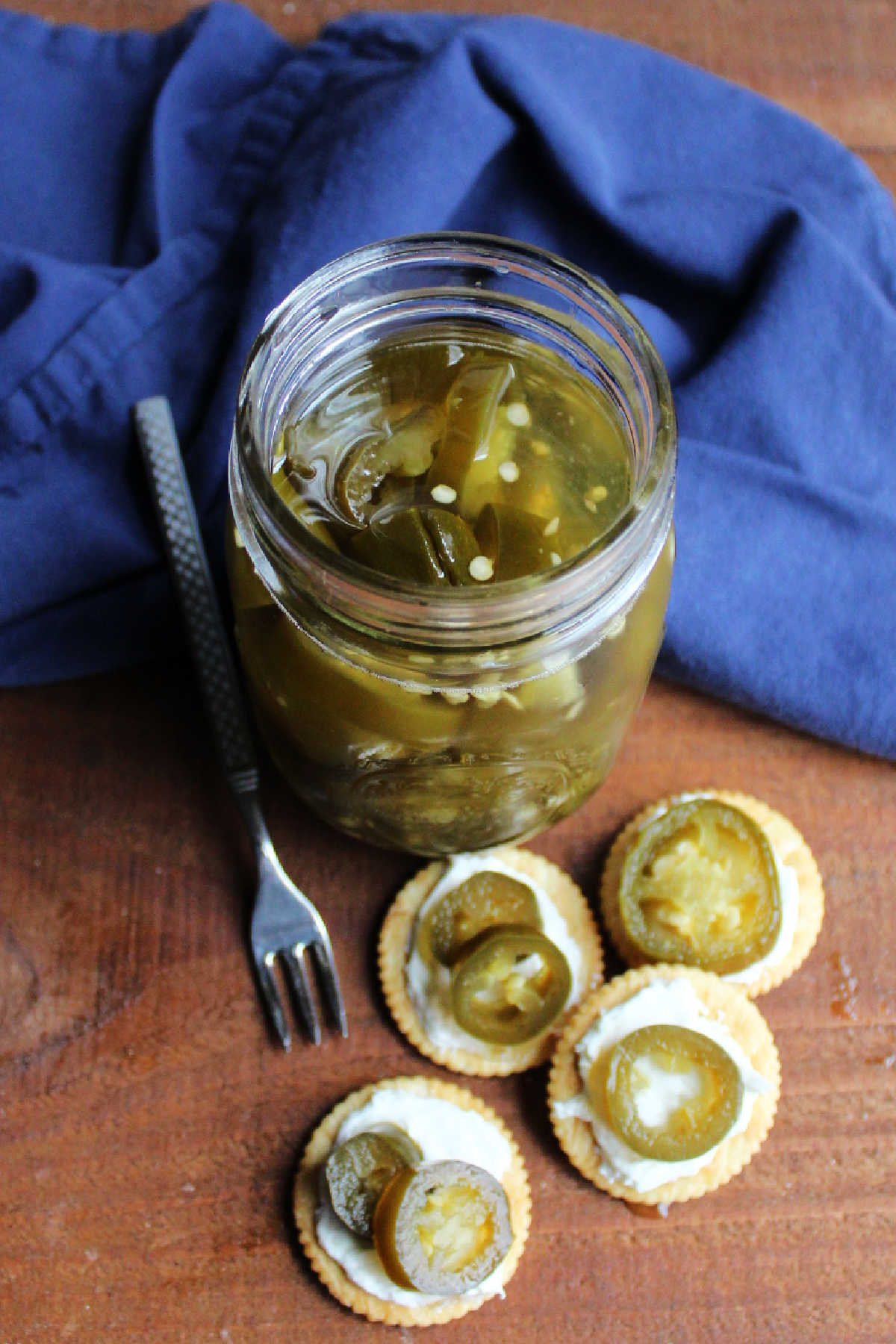 Looking down on a jar of cowboy candy next to crackers topped with cream cheese and candied jalapeno rings.