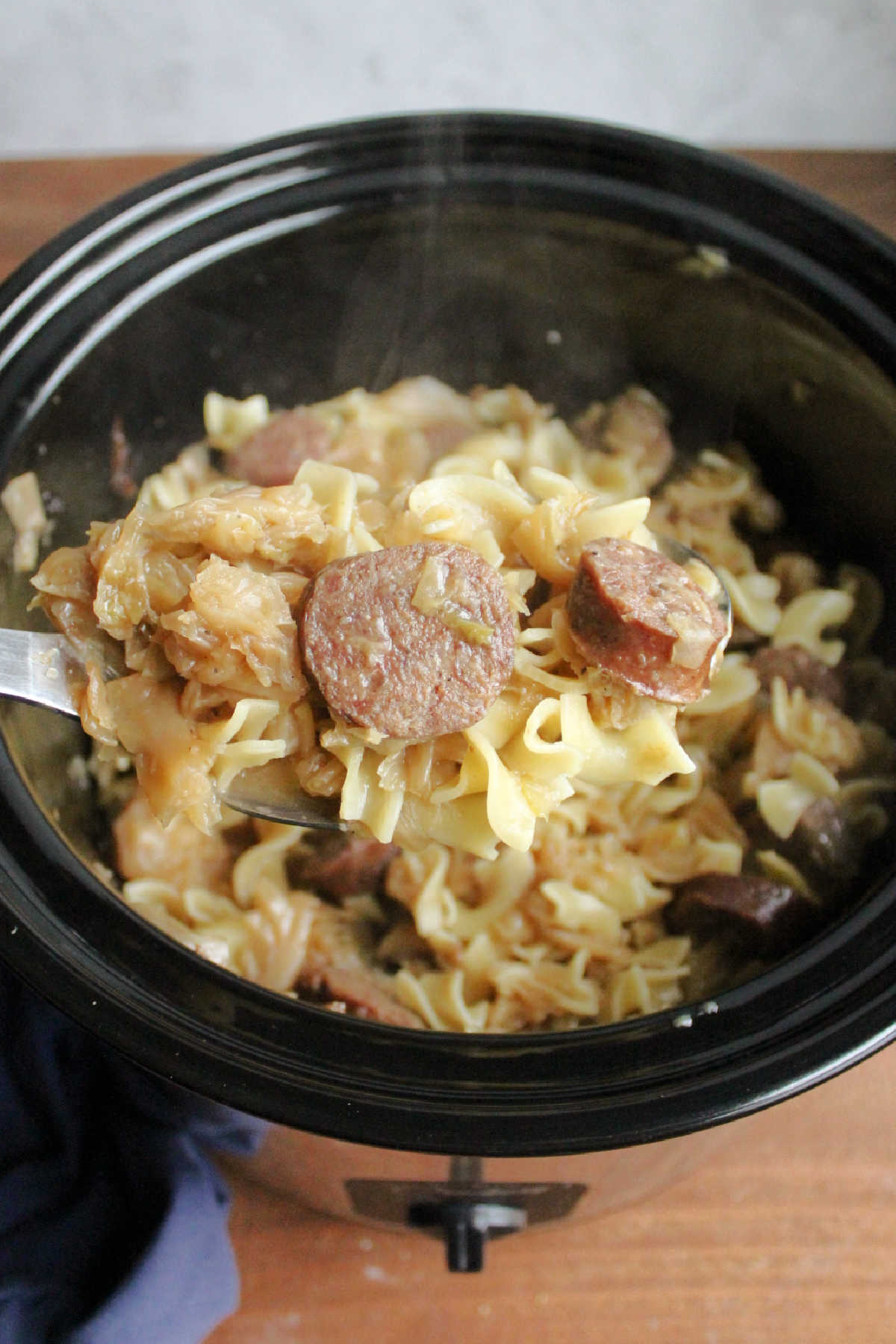 Large spoon filled with slow cooker haluski showing cooked pasta, cabbage, and sausage.