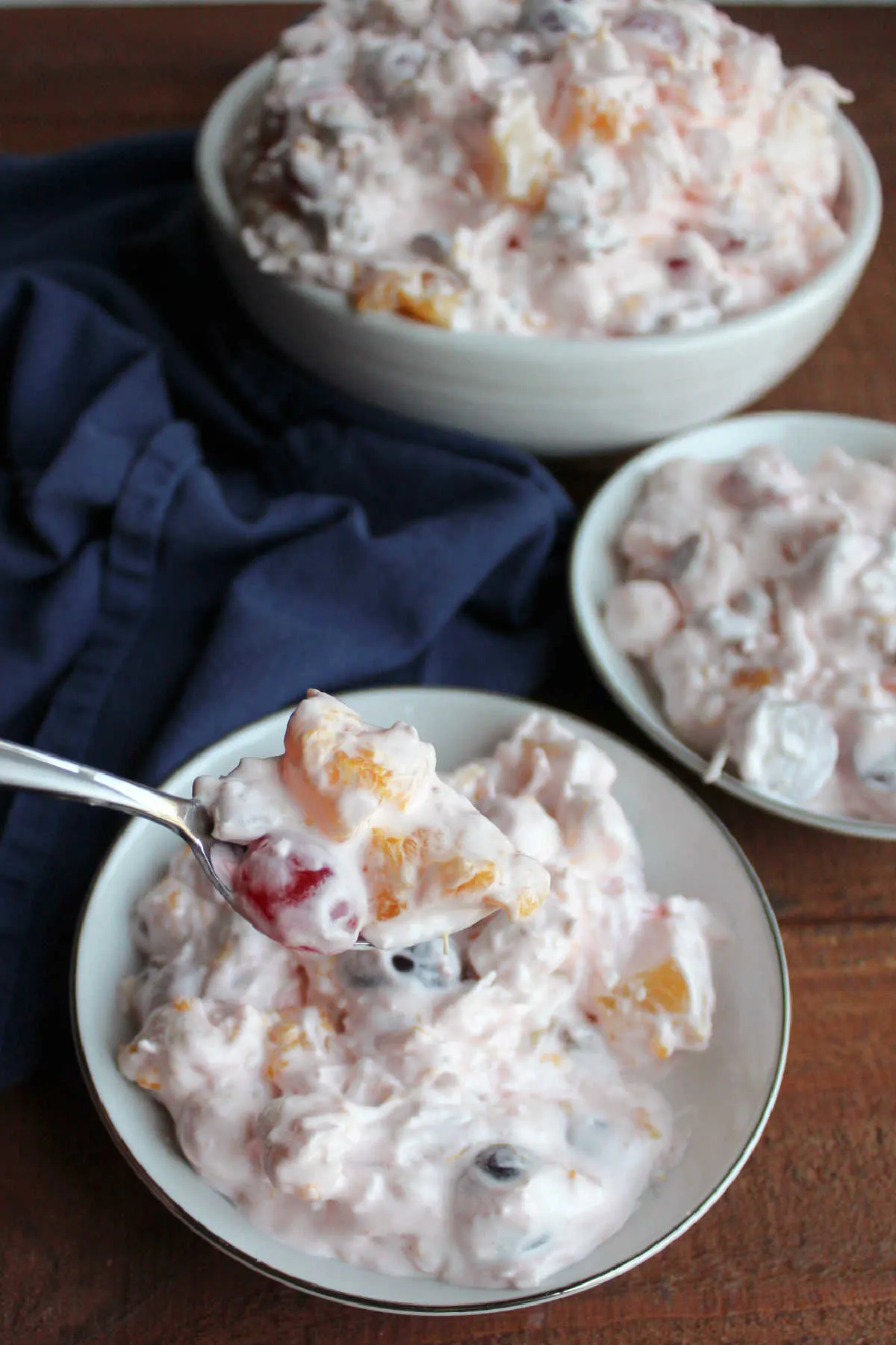 Spoonful of ambrosia fruit salad with orange section, pineapple and cherries in a sweet pink dressing ready to eat. 