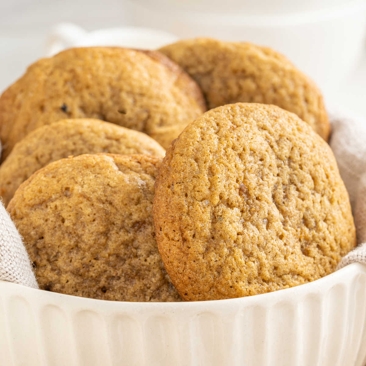 Close up of a white bowl filled with large tan chai spiced cookies, showing their soft texture.