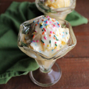 Sundae cup filled with vanilla ice cream topped with a hard shell of white chocolate and colorful sprinkles, ready to eat.