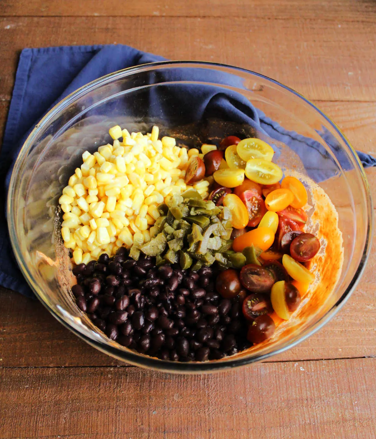 Corn, black beans, halved tomatoes, and chopped jalapenos in bowl with enchilada dressing.