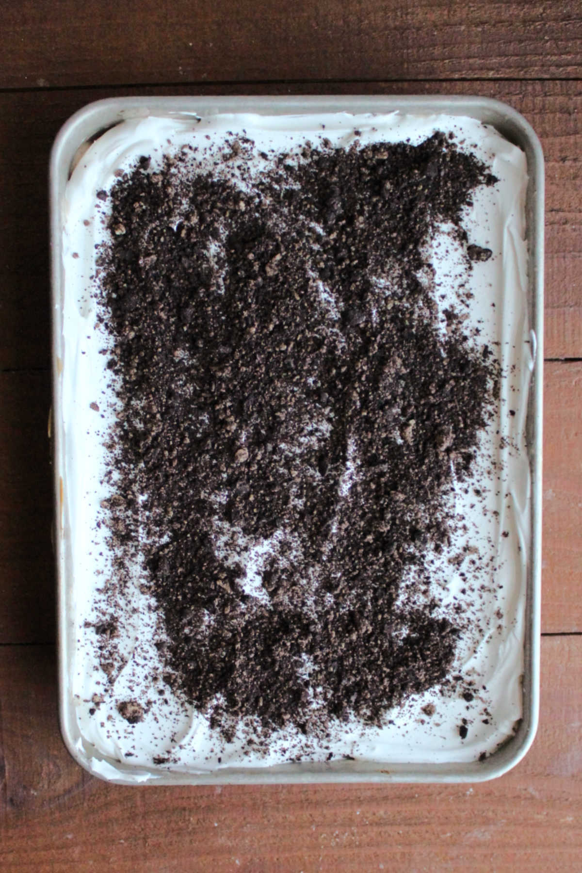 Ice cream cake topped off with whipped topping and cookie crumbs, ready to back in the freezer.