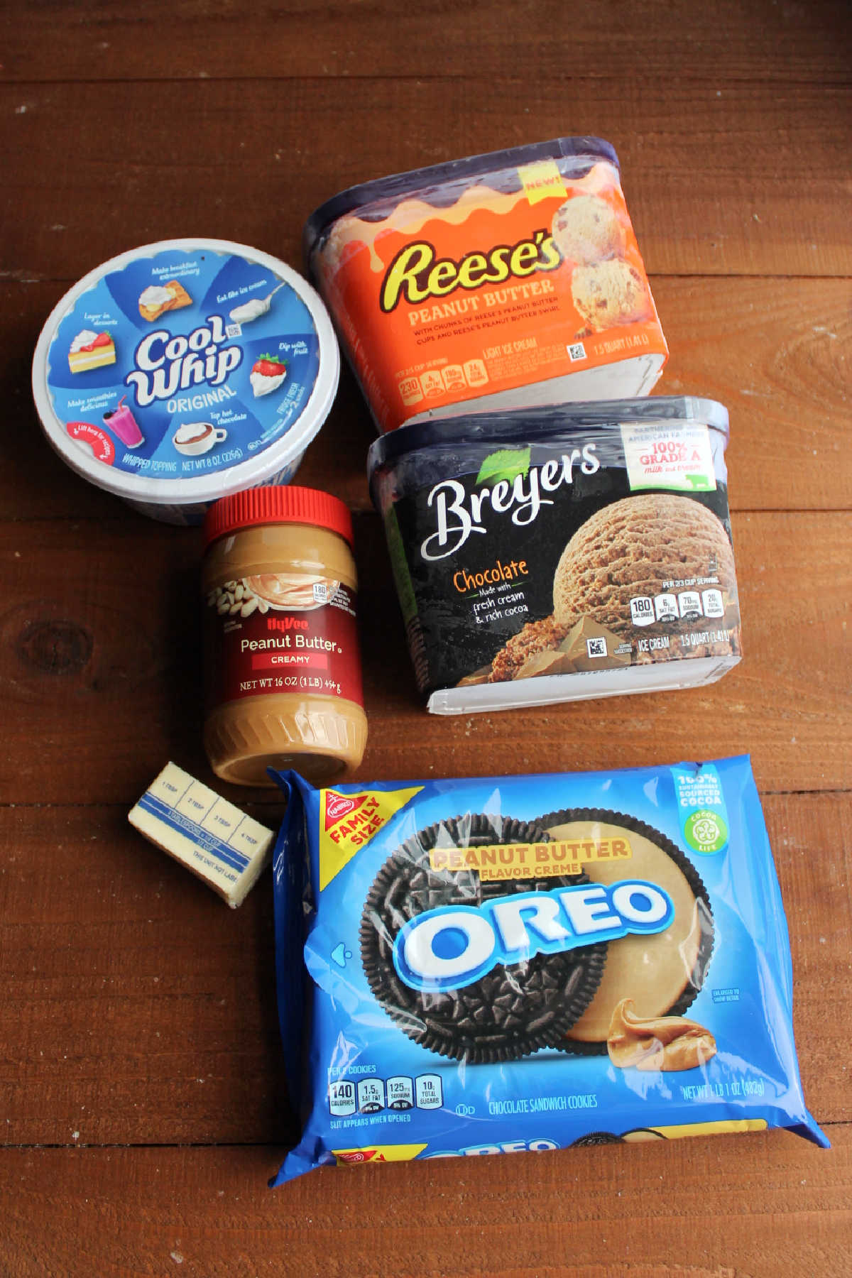 Ingredients including Oreos, butter, peanut butter, Cool Whip, peanut butter ice cream, and chocolate ice cream ready to be layered into an ice cream cake.