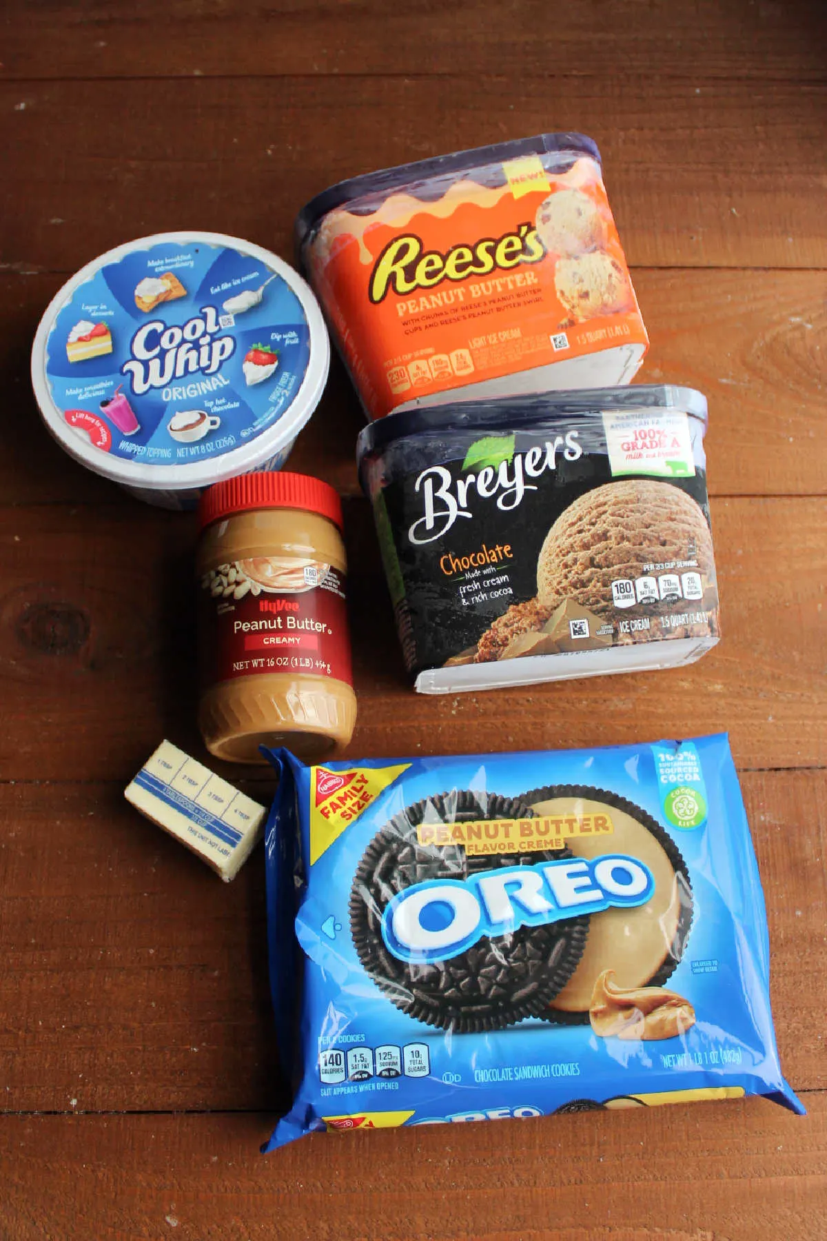 Ingredients including Oreos, butter, peanut butter, Cool Whip, peanut butter ice cream, and chocolate ice cream ready to be layered into an ice cream cake.