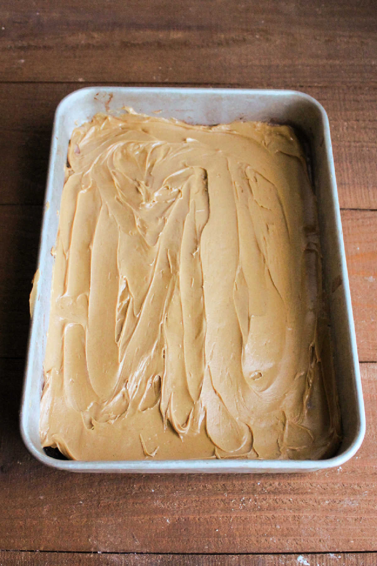 Creamy peanut butter spread over chocolate ice cream in cake pan.
