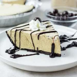 Slice of creamy frozen coffee pie drizzled with hot fudge sauce and topped with a little bit of whipped cream and a chocolate covered espresso bean.