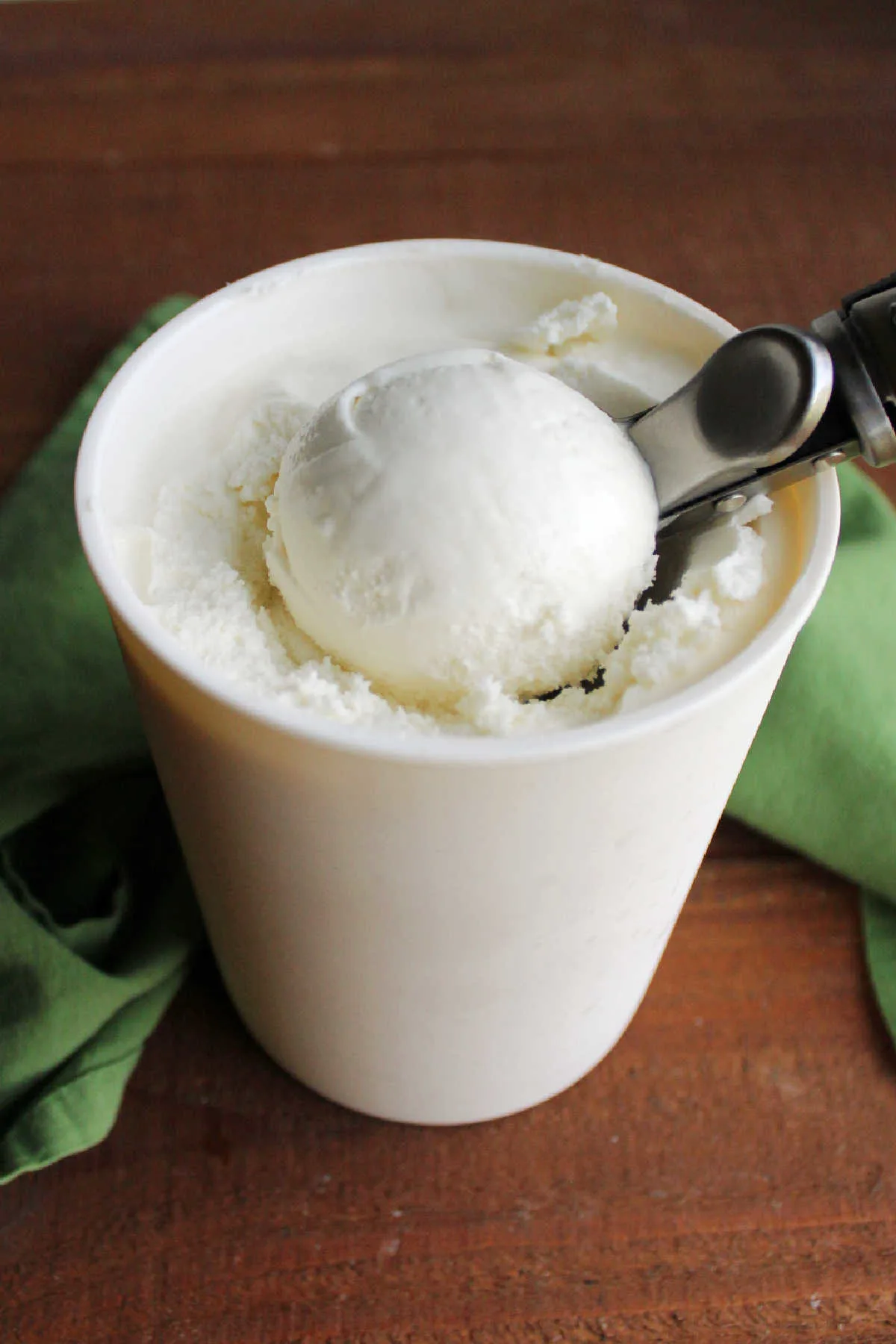 Ice cream scoop getting ball of key lime ice cream from quart storage container.