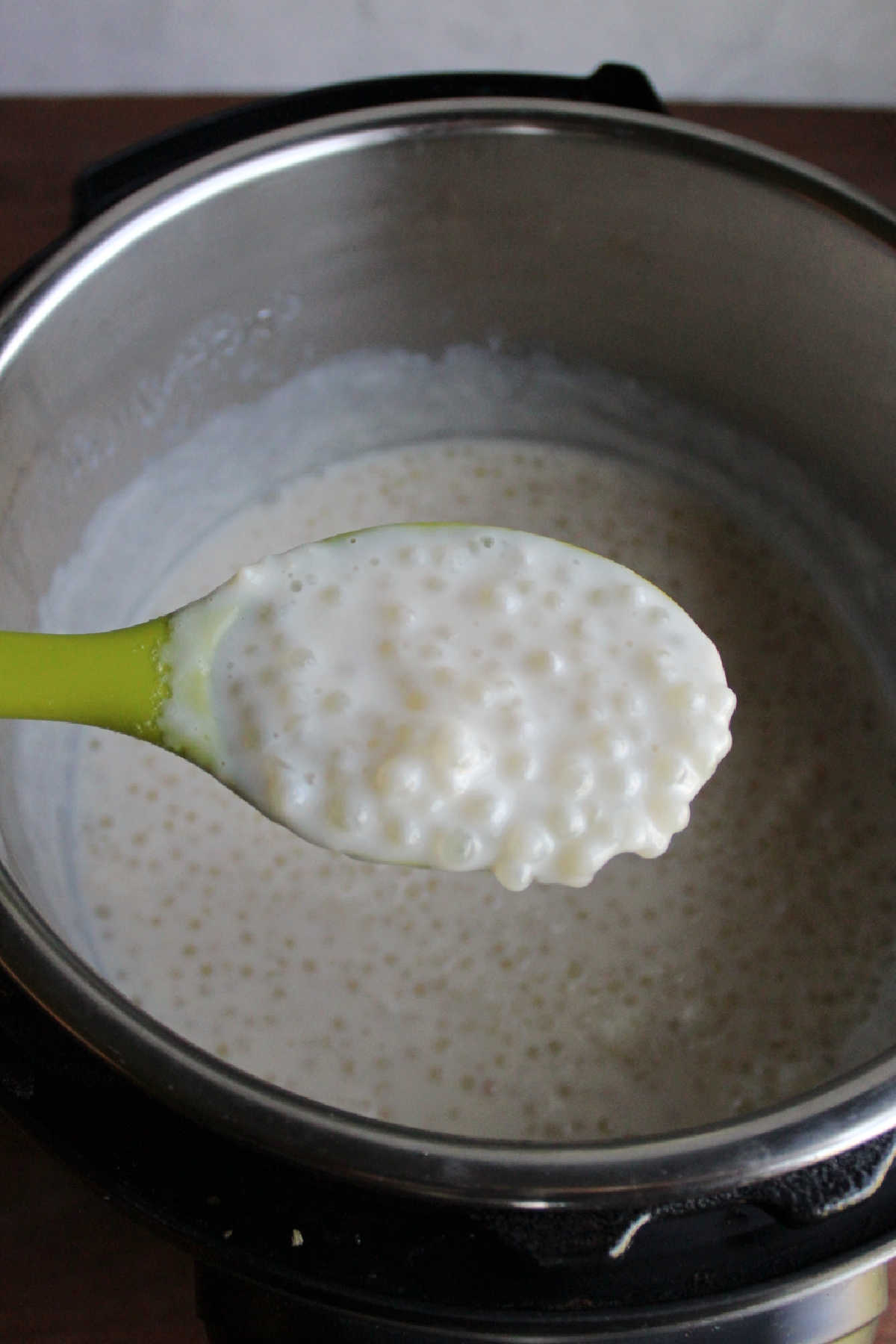 Large spoon with a scoop of warm tapioca over the instant pot with the remaining tapioca.