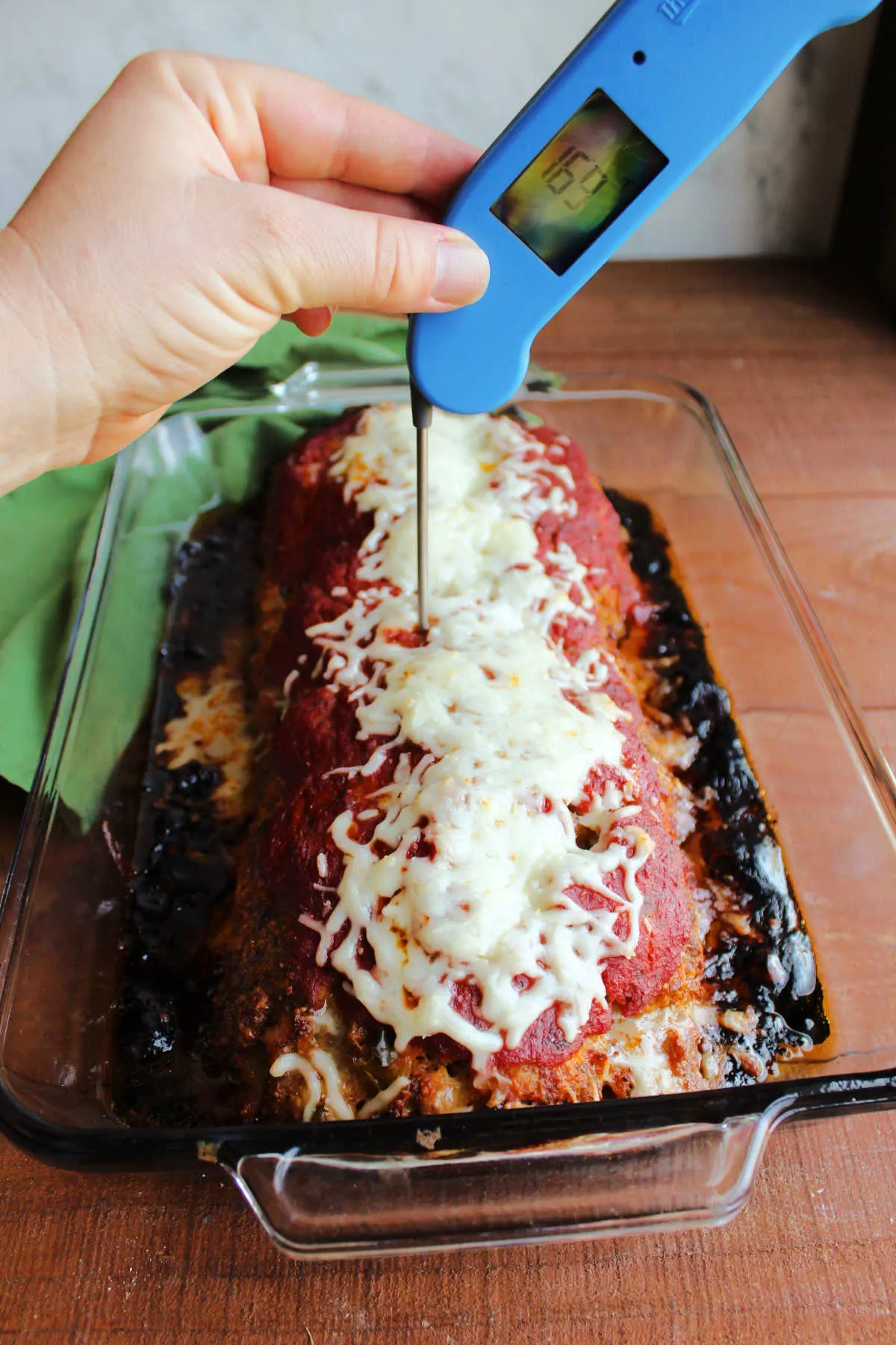Meat thermometer in a baked Italian meatloaf topped with melted cheese. 