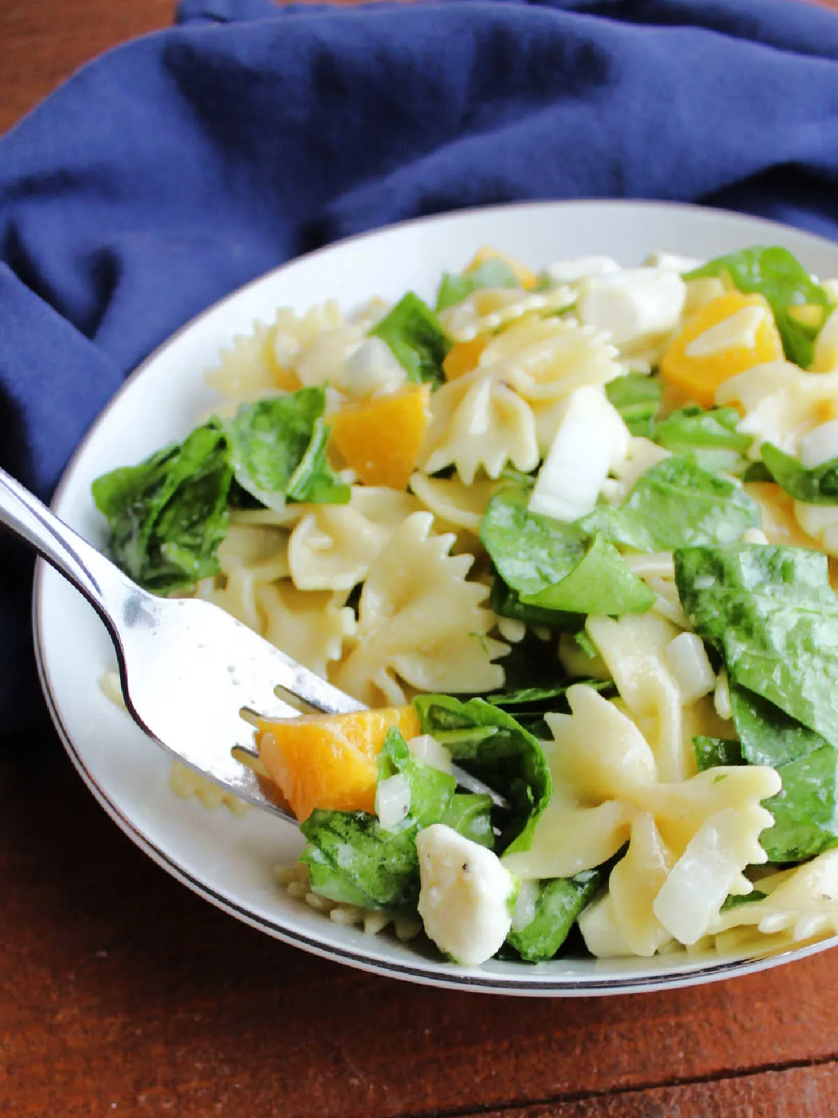Bite of peach pasta salad with fresh spinach and a mozzarella pearl on fork.