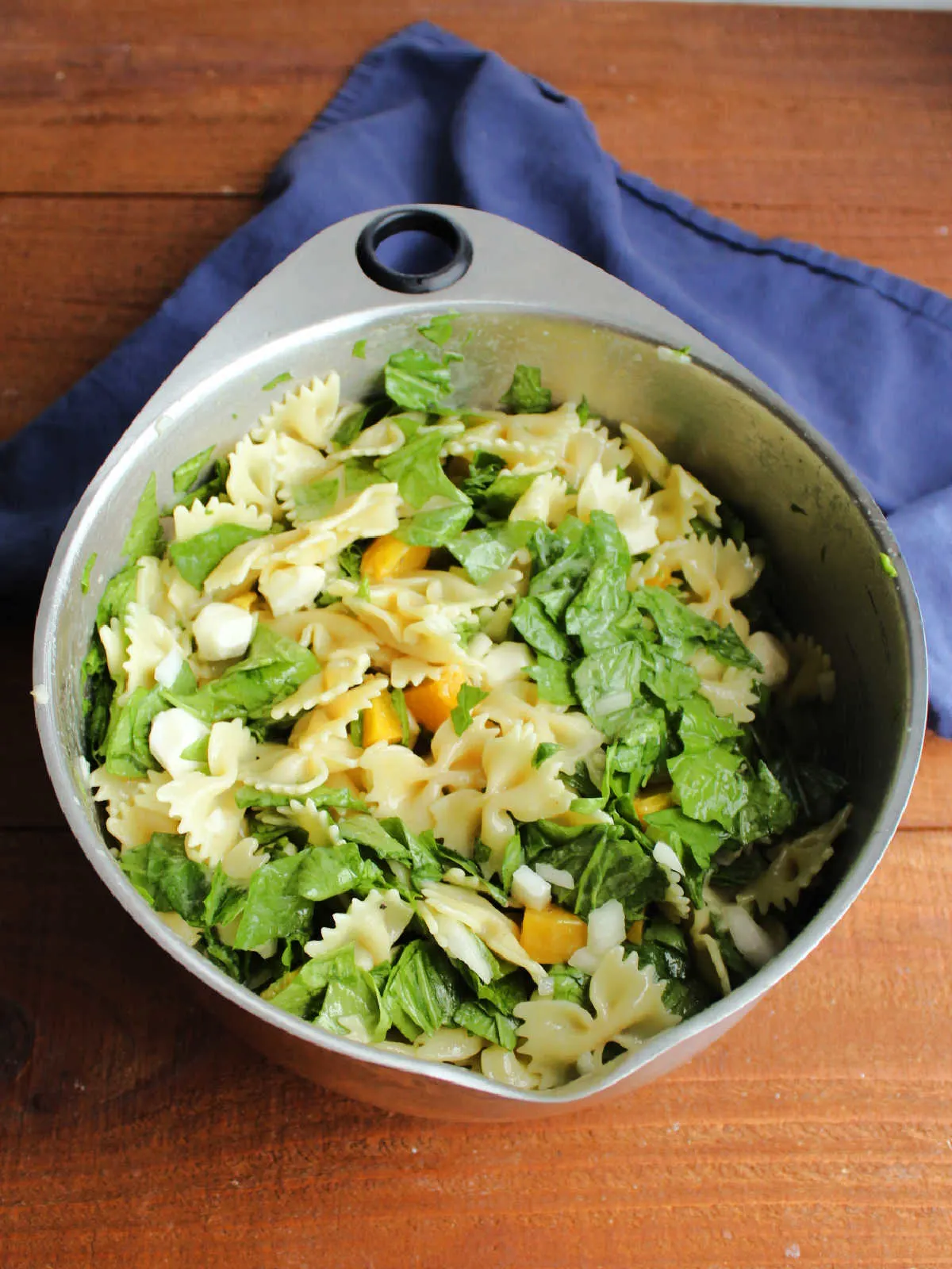 Large mixing bowl filled with peach pasta salad with spinach and cheese, ready to be served.