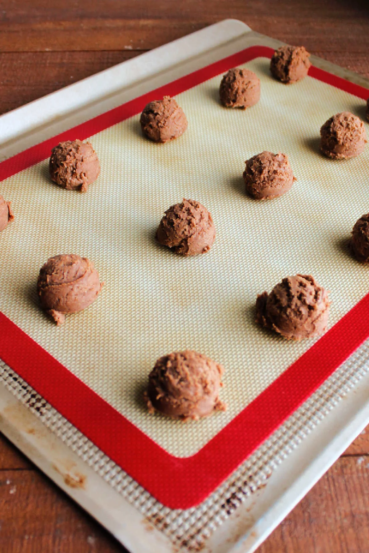 Small scoops of chocolate cookie dough on silicone mat lined cookie sheet.