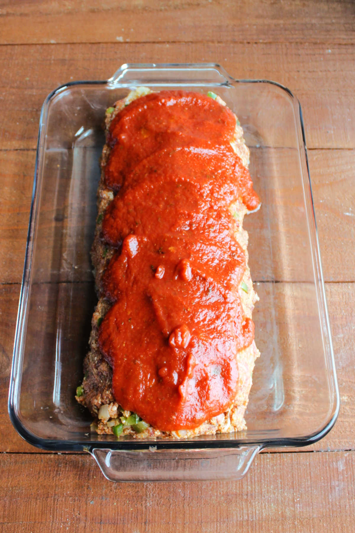 Marinara sauce on top of raw meatloaf in pan, ready to go in the oven.