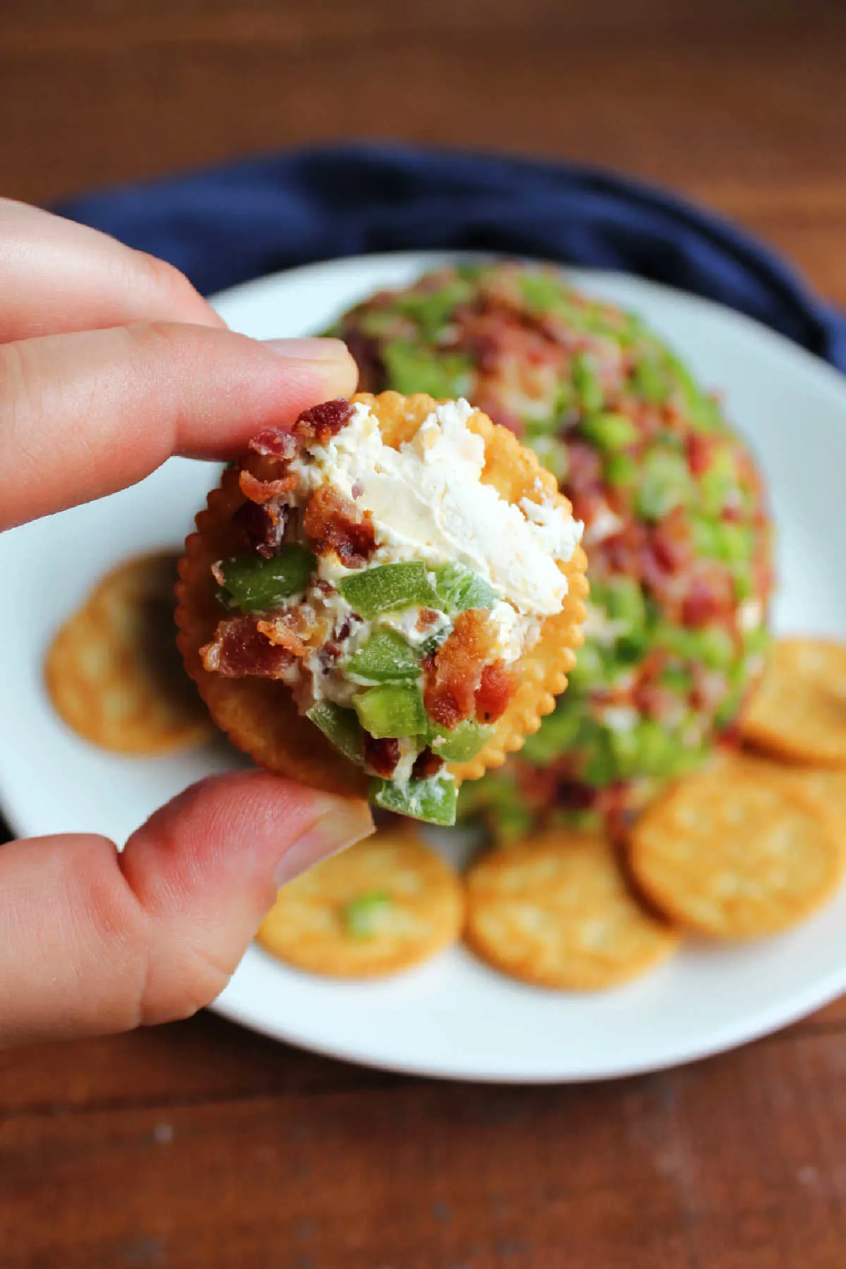 Hand holding cracker with bacon jalapeno cheese ball spread over the top.