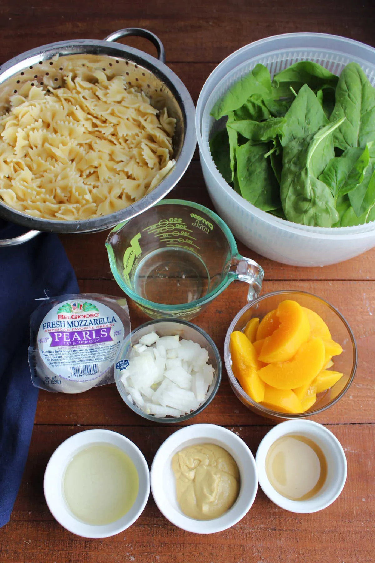 Ingredients including pasta, spinach, peaches, mustard, oil, vinegar, and diced onion.