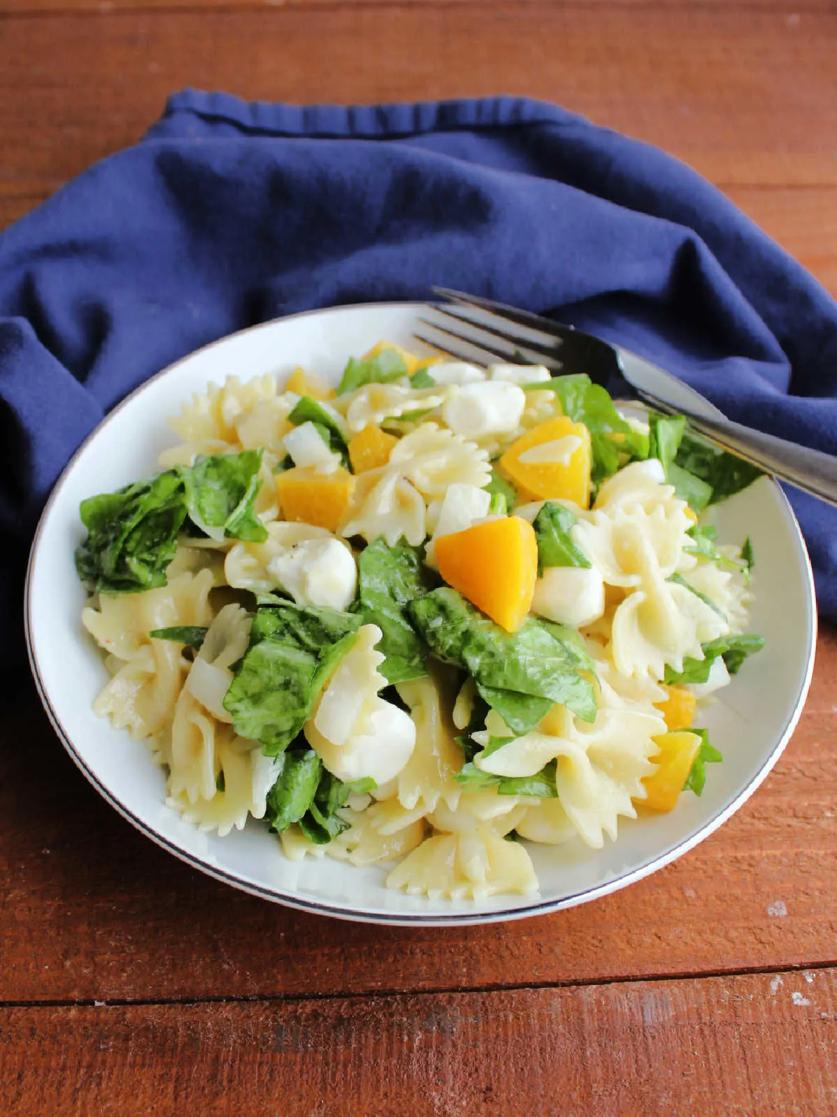 Bowl of peach pasta salad with spinach, ready to eat.