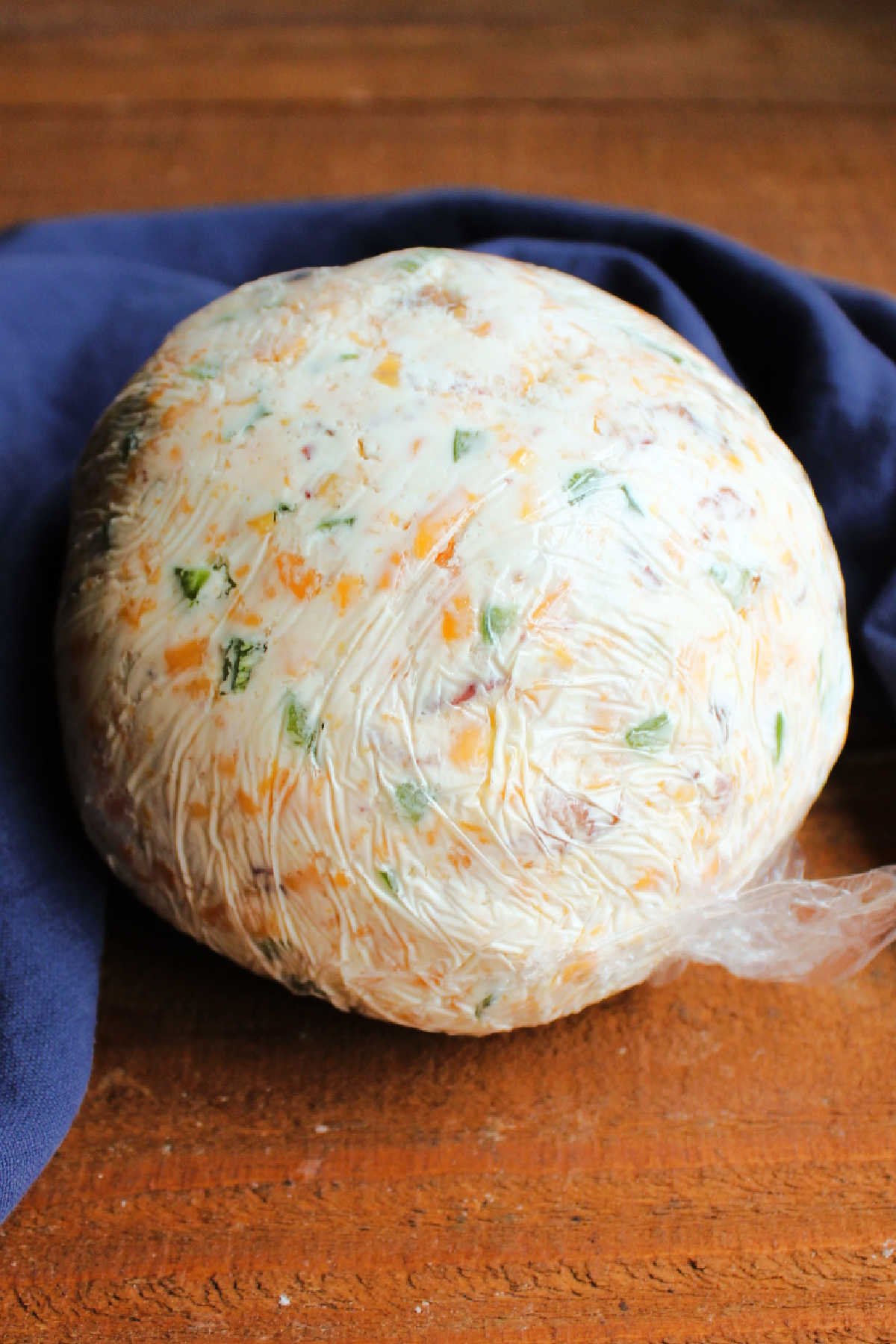 Bacon and jalapeno cheese ball wrapped in plastic wrap, ready to go in the refrigerator.
