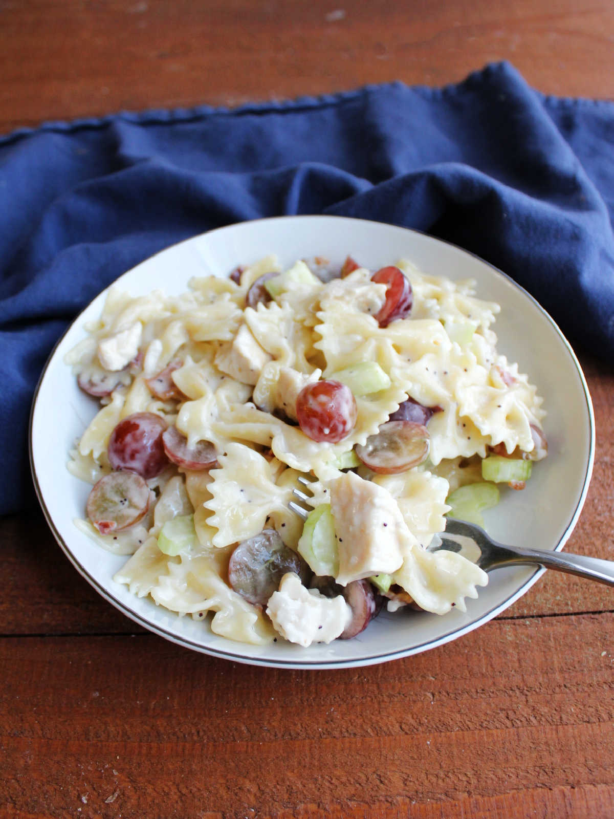 Bowl of chicken poppy seed macaroni salad with red grapes, bacon, and celery.