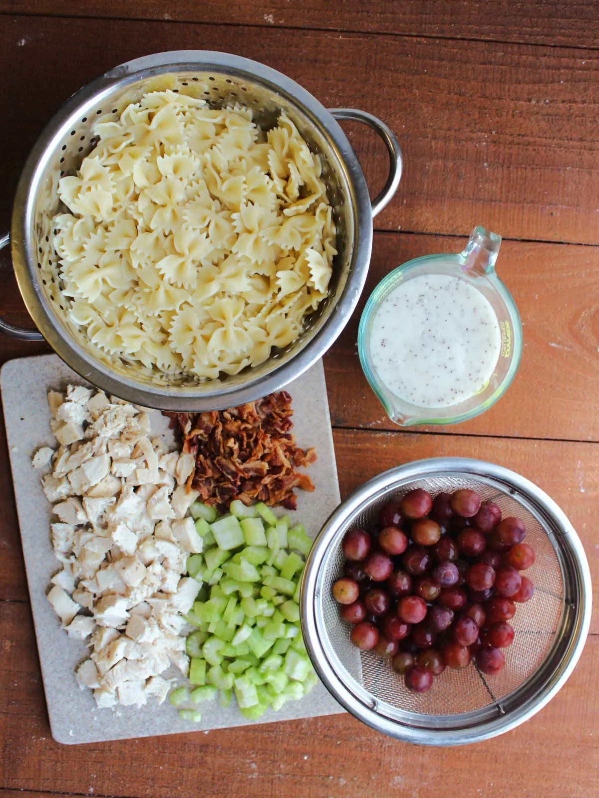 Ingredients for poppy seed pasta salad including cooked pasta, creamy poppy seed dressing, washed grapes, chopped celery, crumbled bacon, and cooked chicken.