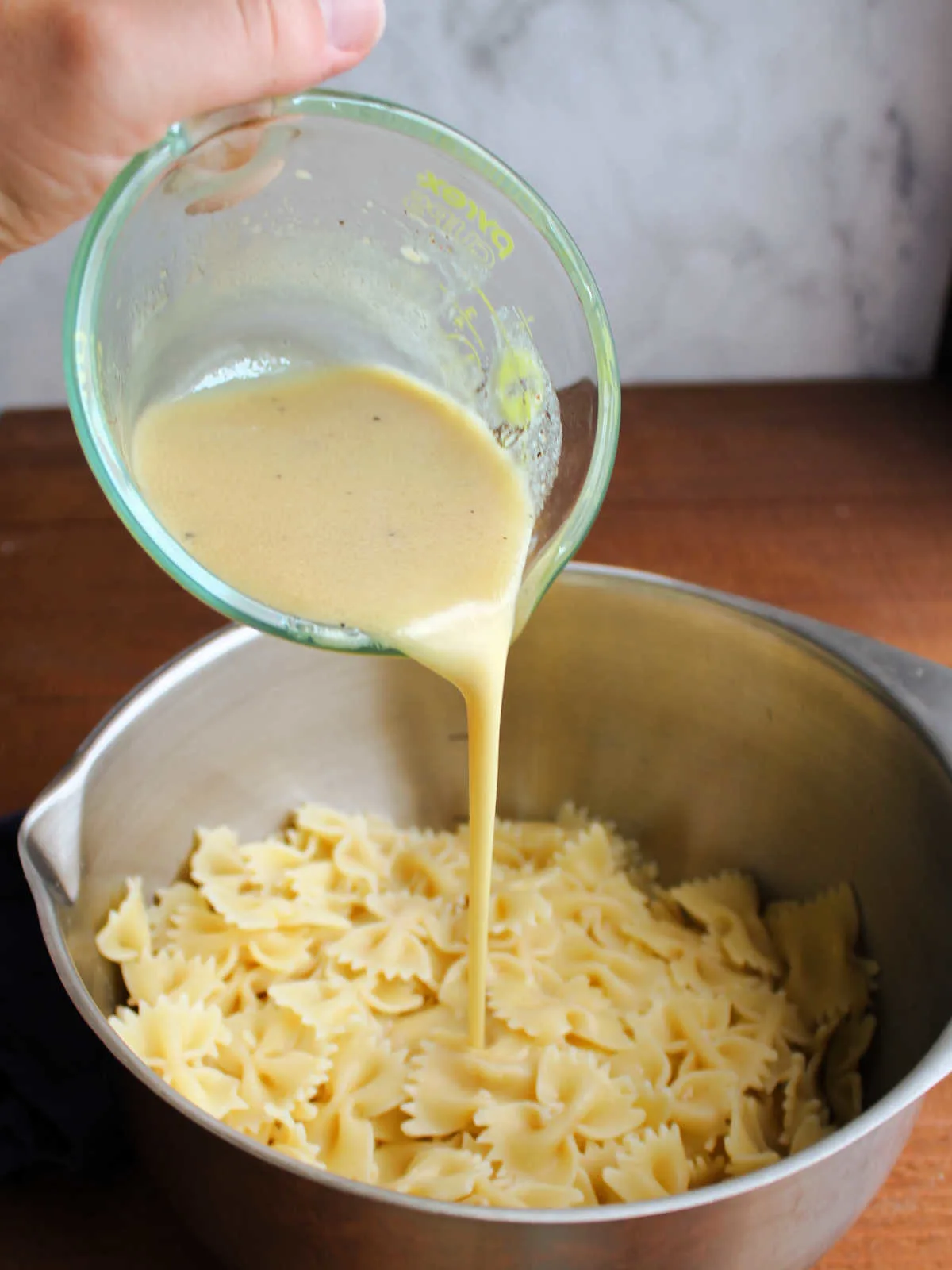Pouring homemade peach mustard dressing over a bowl of al dente pasta.