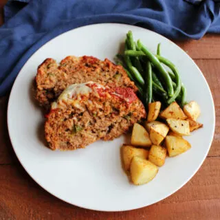 Dinner plate with two slices of Italian sausage meatloaf, roasted potatoes, and roasted green beans.