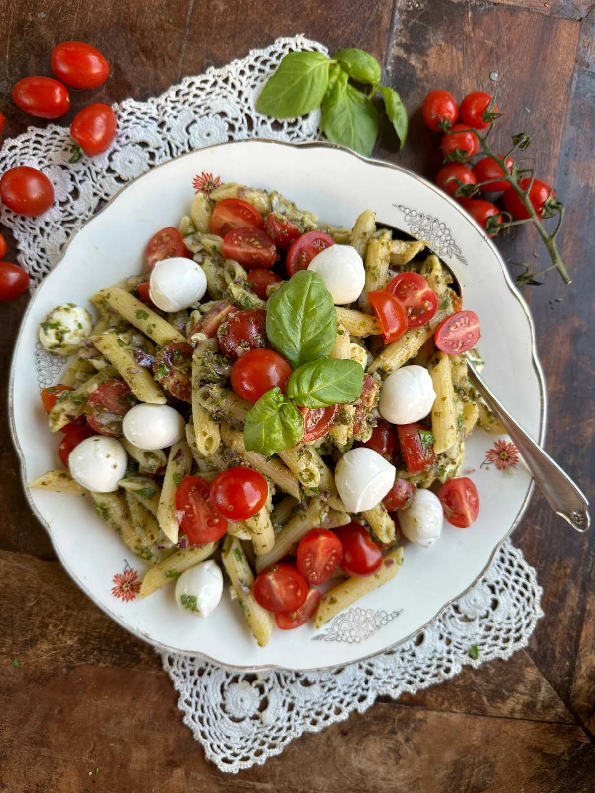 Plate filled with pesto penne salad with cheese, basil, and tomatoes.