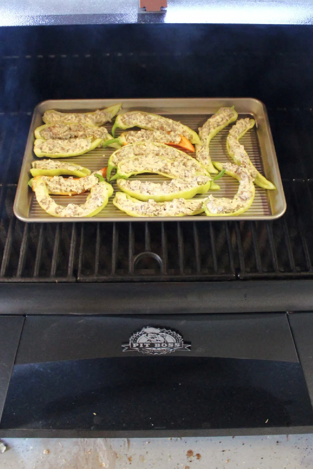 Tray of stuffed banana peppers on pellet grill grate. 