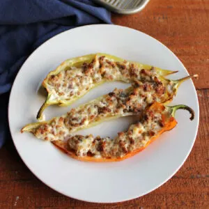 Small white plate with three stuffed banana pepper halves filled with cream cheese and sausage.
