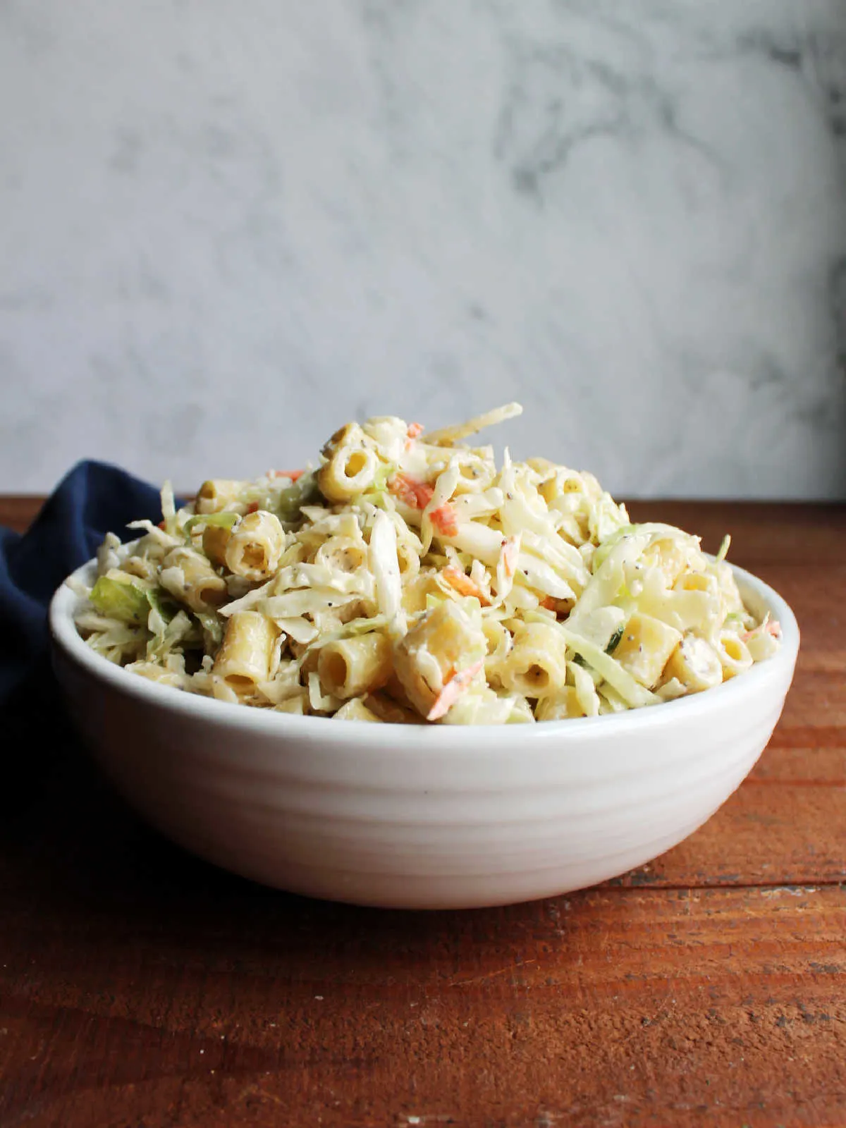 White serving bowl piled high with creamy coleslaw pasta salad, ready to eat. 