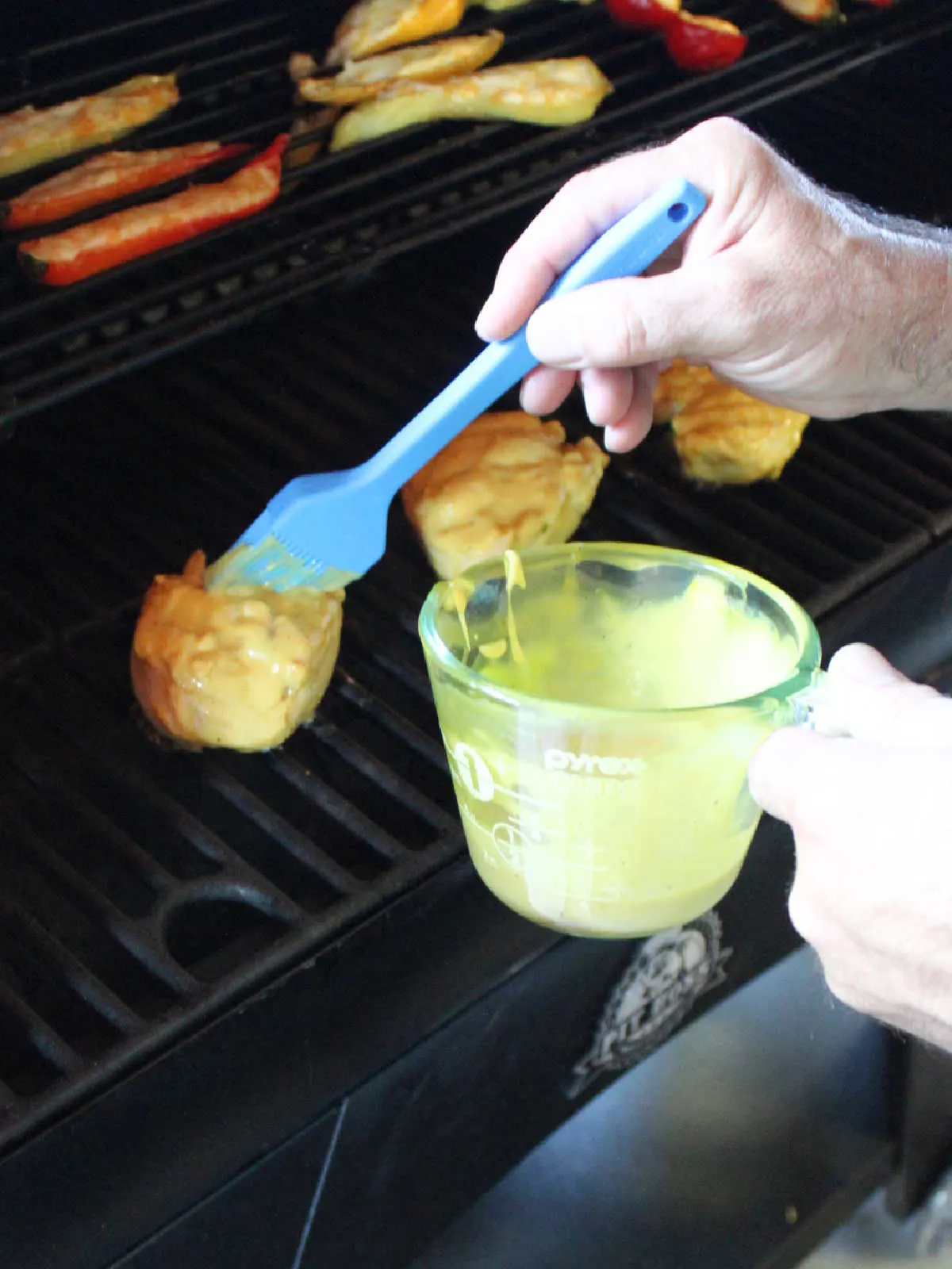 Brushing yellow mustard ranch sauce over chicken breasts on the pellet grill.