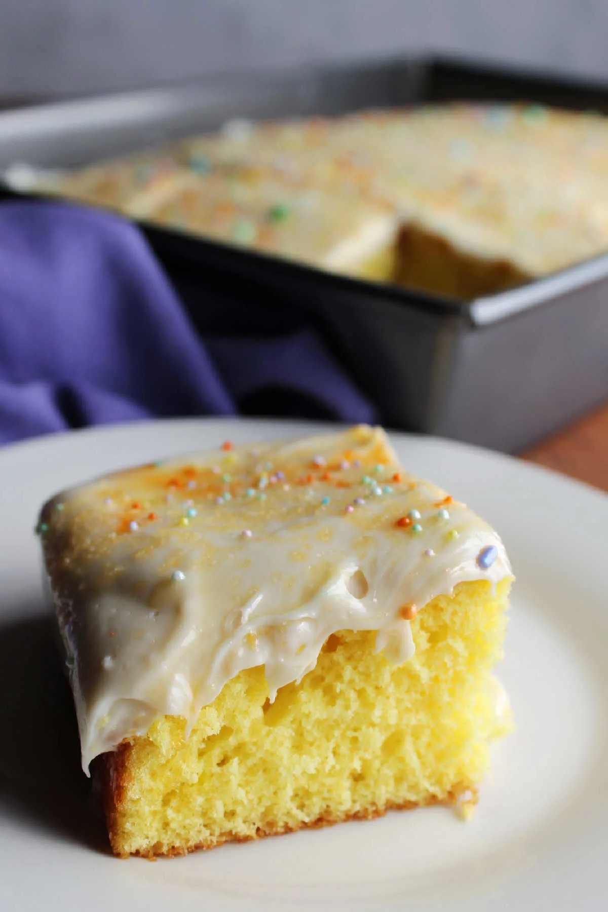 Close up of a piece of lemon cake topped with creamy lemon cream cheese frosting and colorful sprinkles. 