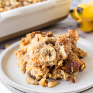 Close up serving of banana bread pudding with slices of bananas and chopped walnuts.